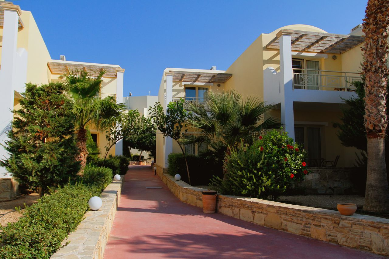Charming Mediterranean villas with lush palm trees and gardens under a bright blue sky.