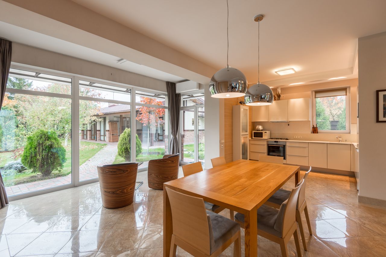 Interior of modern cottage made in minimalist style with wooden furniture in dining zone and convenient kitchen with built in appliances